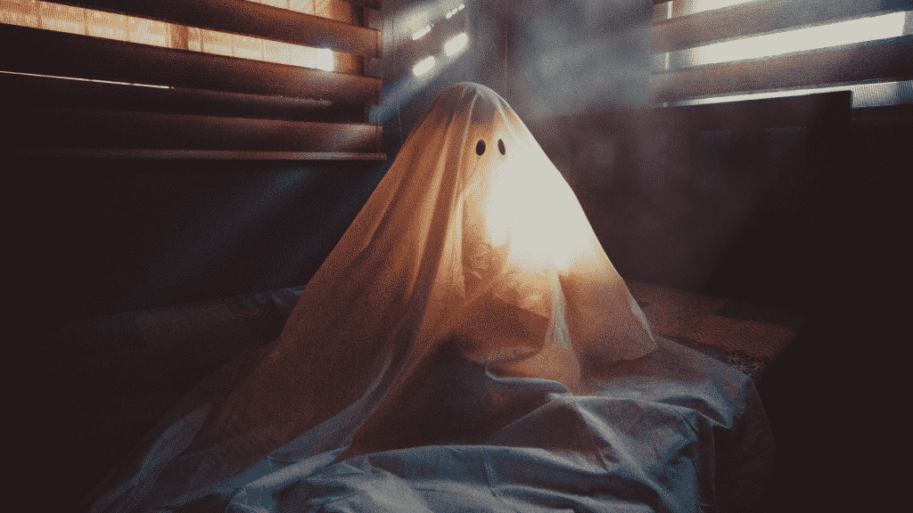 Fantasma de lençol sentado sobre cama