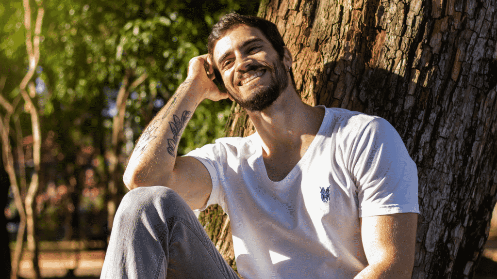 Homem sorridente sentado embaixo de uma árvore