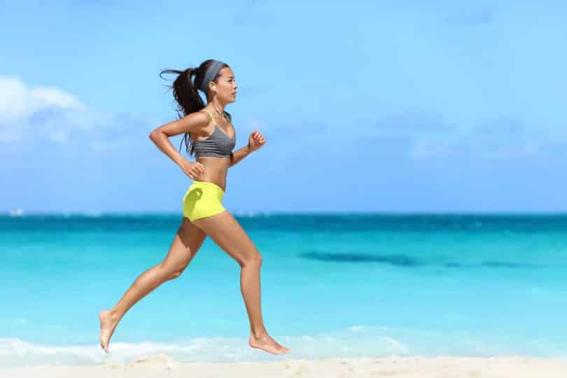 Mulher corre em praia, à beira mar.