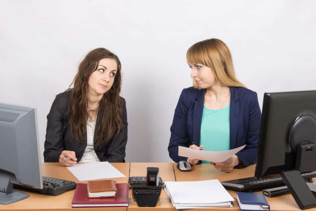 Mulheres brancas num escritório se estranhando.