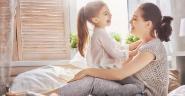 Menina branca sentada no colo de mulher branca na cama.