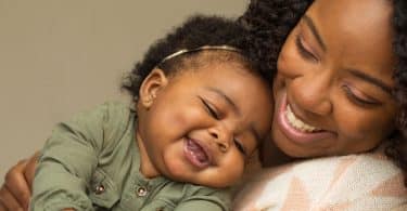 Mulher segura bebê. Ambos riem.