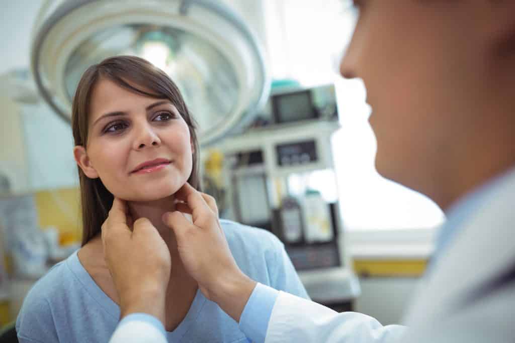 Médico branco com as mãos no pescoço de uma mulher branca.