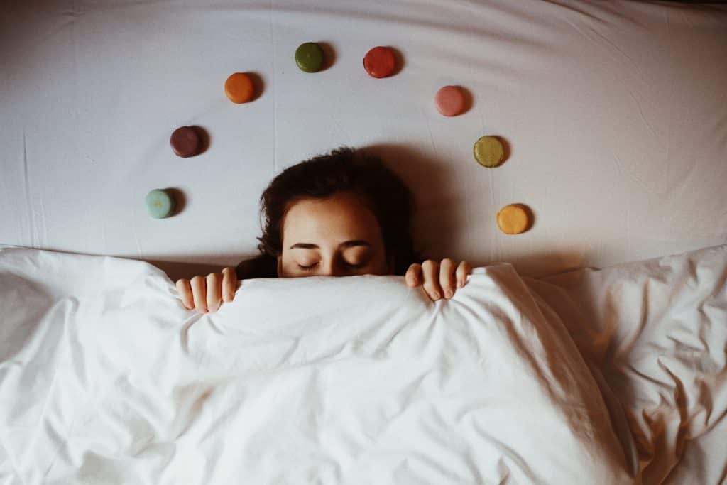 Mulher branca deitada numa cama com pedras coloridas no travesseiro.