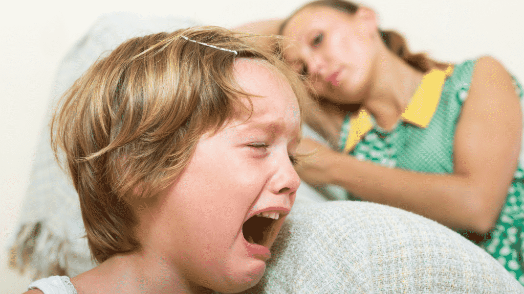 Imagem de uma criança chorando e uma mulher ao fundo