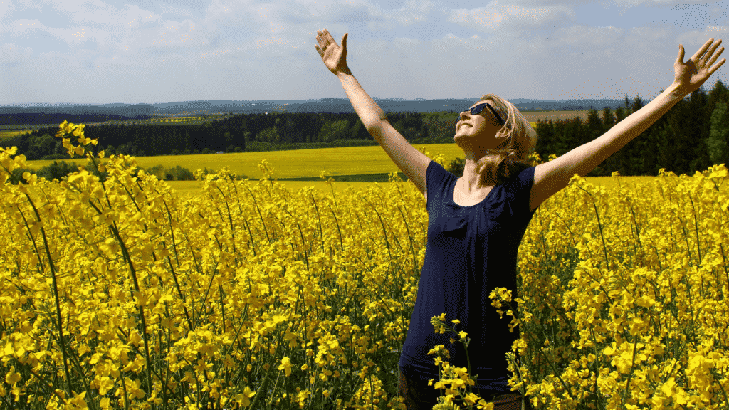 Mulher no meio de um campo de flores de braços abertos e olhando para o céu