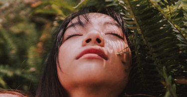 Mulher asiática com os olhos fechados perto de plantas.