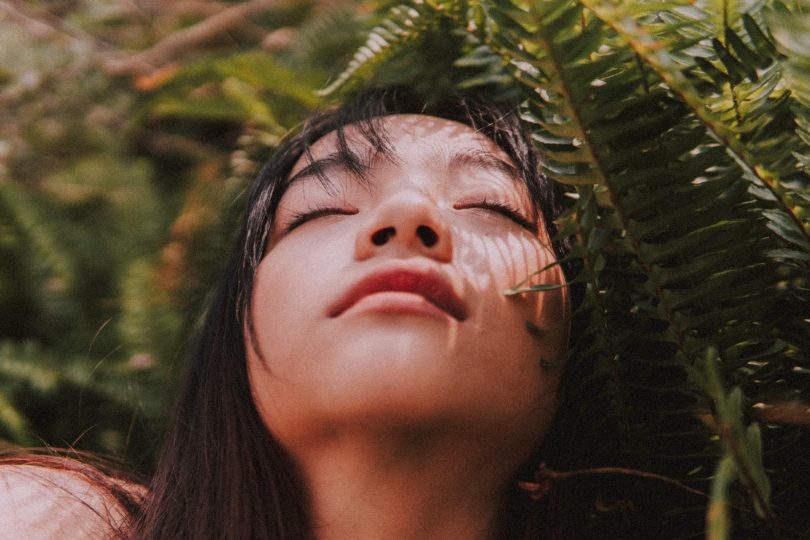 Mulher asiática com os olhos fechados perto de plantas.