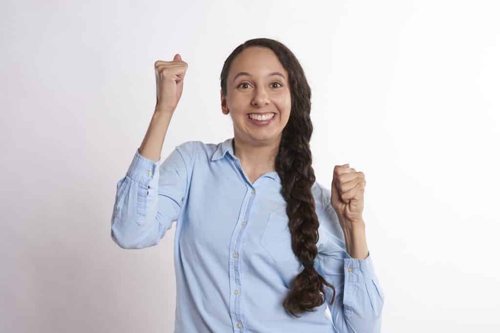 Imagem de uma mulher de cabelos longos e castanhos. Ela usa uma trança. Veste uma camisa azul clara. Ela está confiante, otimista e resiliente.