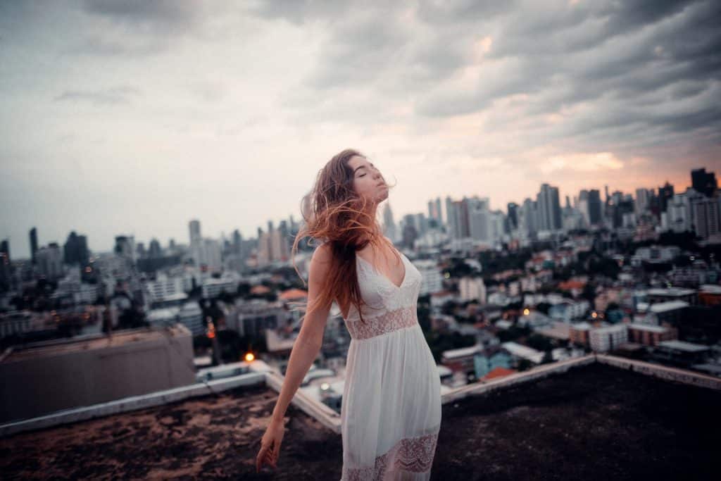 Mulher branca de olhos fechados no topo de um prédio.