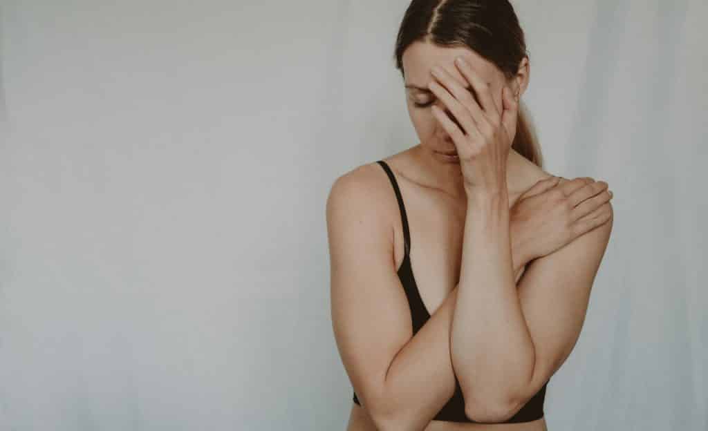 Mulher com o rosto virado e a mão sobre ele. Ela abraça o próprio corpo.
