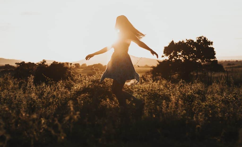 Mulher em movimento giratório em campo. Ao fundo, há o Sol.