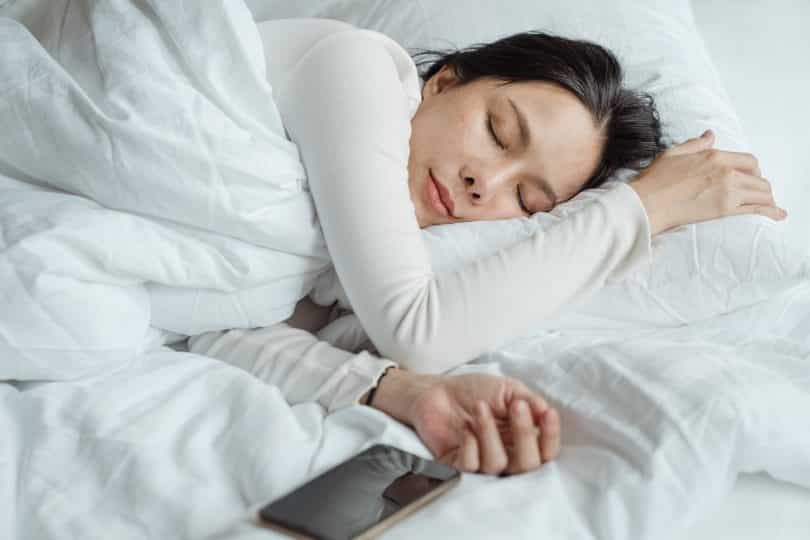 Mulher dormindo de lado em uma cama com lençóis brancos