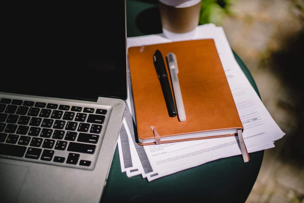 Duas canetas em cima de uma agenda com um laptop ao lado