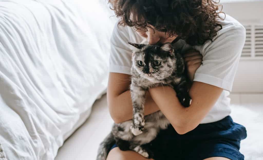 Mulher sentada no chão abraça gato. 