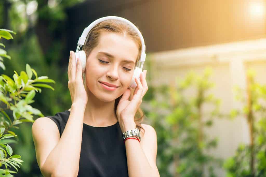 Mulher com os olhos fechados ouve música em fones de ouvido brancos.