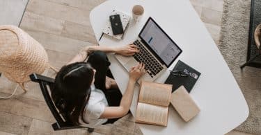 Mulher estudando em frente a um computador com livros ao seu lado