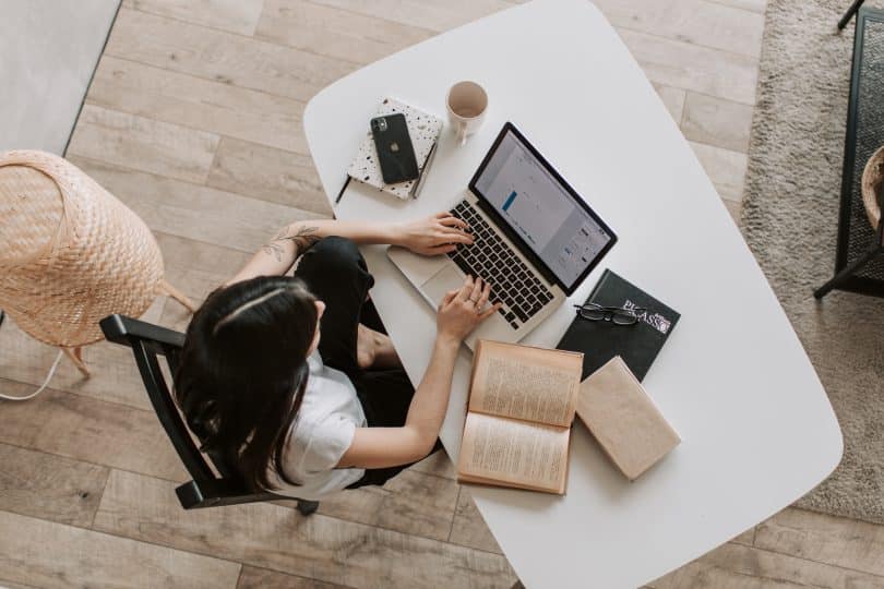 Mulher estudando em frente a um computador com livros ao seu lado