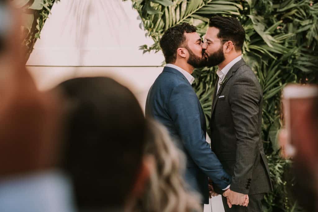 Dois homens brancos se beijando no casamento.