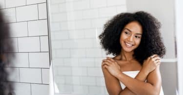 Mulher negra se abraçando em frente ao espelho.