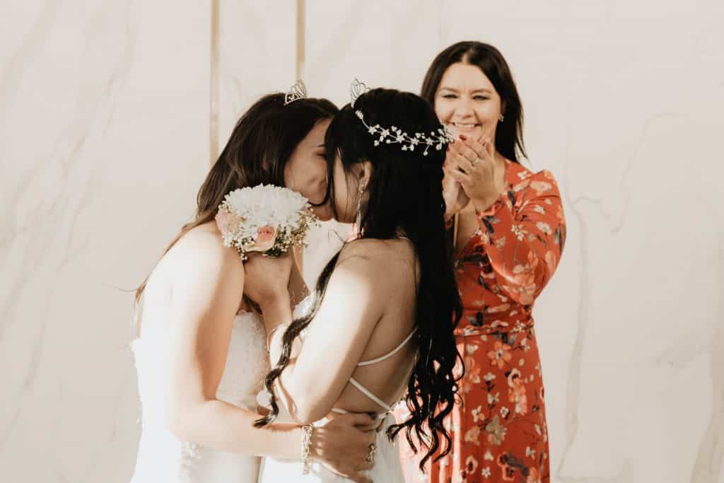 Duas mulheres brancas se beijando no casamento.
