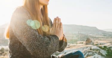 Mulher em prática meditativa em ambiente externo e solar, além de montanhoso.