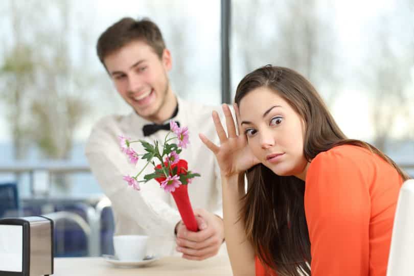 Mulher recusa homem que lhe dá flores. Ambos estão sentados à mesa.
