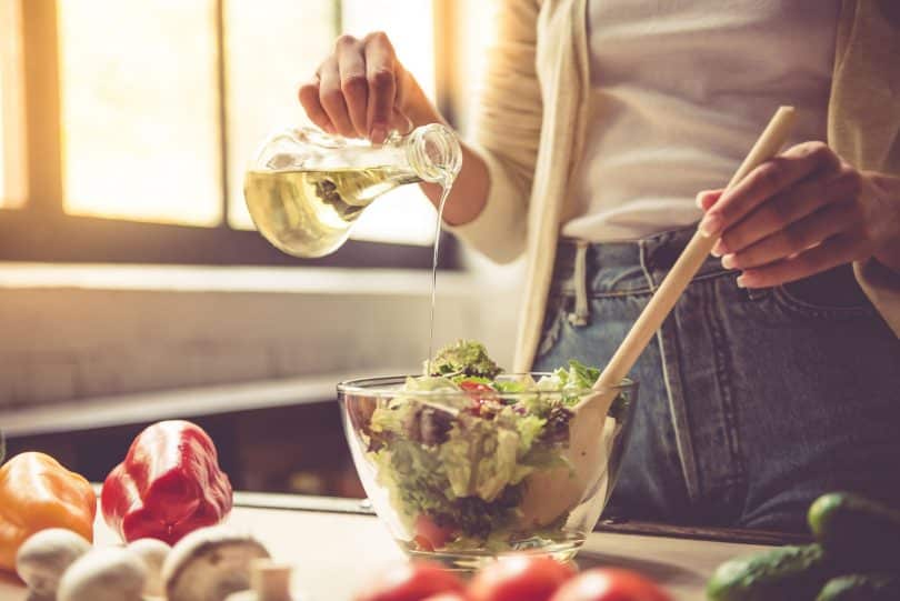 Mulher branca regando salada com azeite.