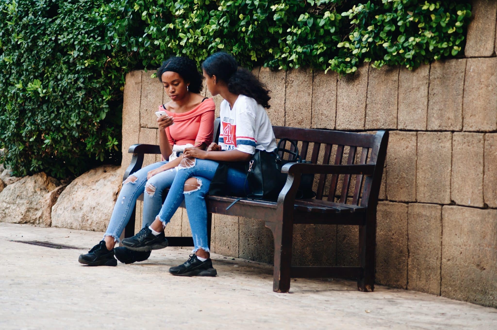 Duas jovens negras sentadas num banco conversando.