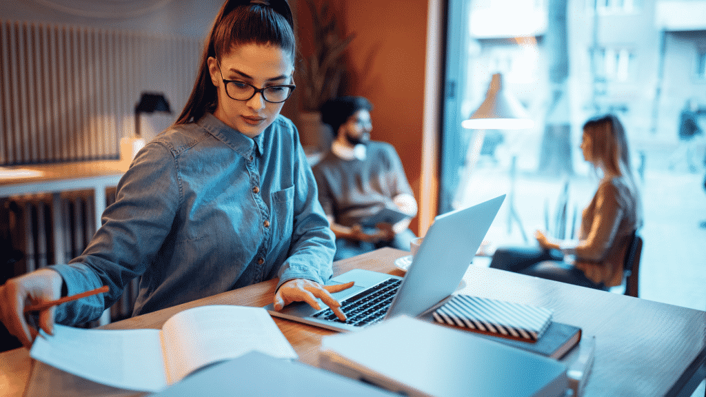 Mulher estudando em um espaço público, utilizando notebook e caderno