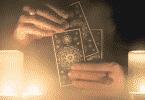 Pessoa manuseando cartas de Tarot em uma mesa. Duas velas acesas encontram-se ao lado.