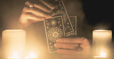 Pessoa manuseando cartas de Tarot em uma mesa. Duas velas acesas encontram-se ao lado.