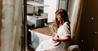 Mulher branca tocando cavaquinho na janela.