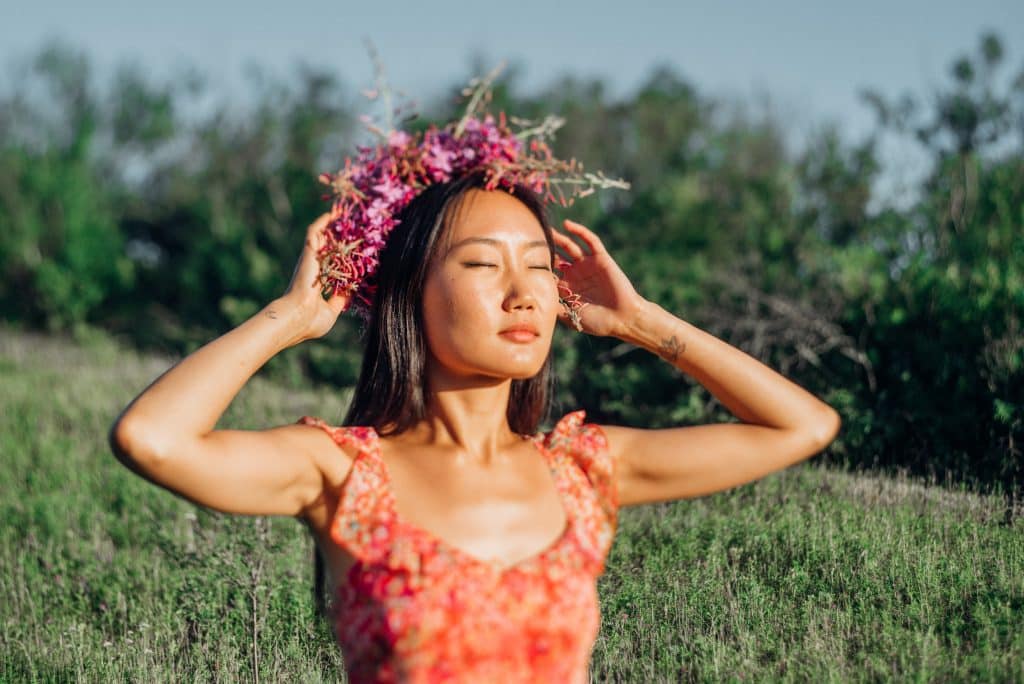 Mulher asiática sendo iluminada pelo sol com os olhos fechados.