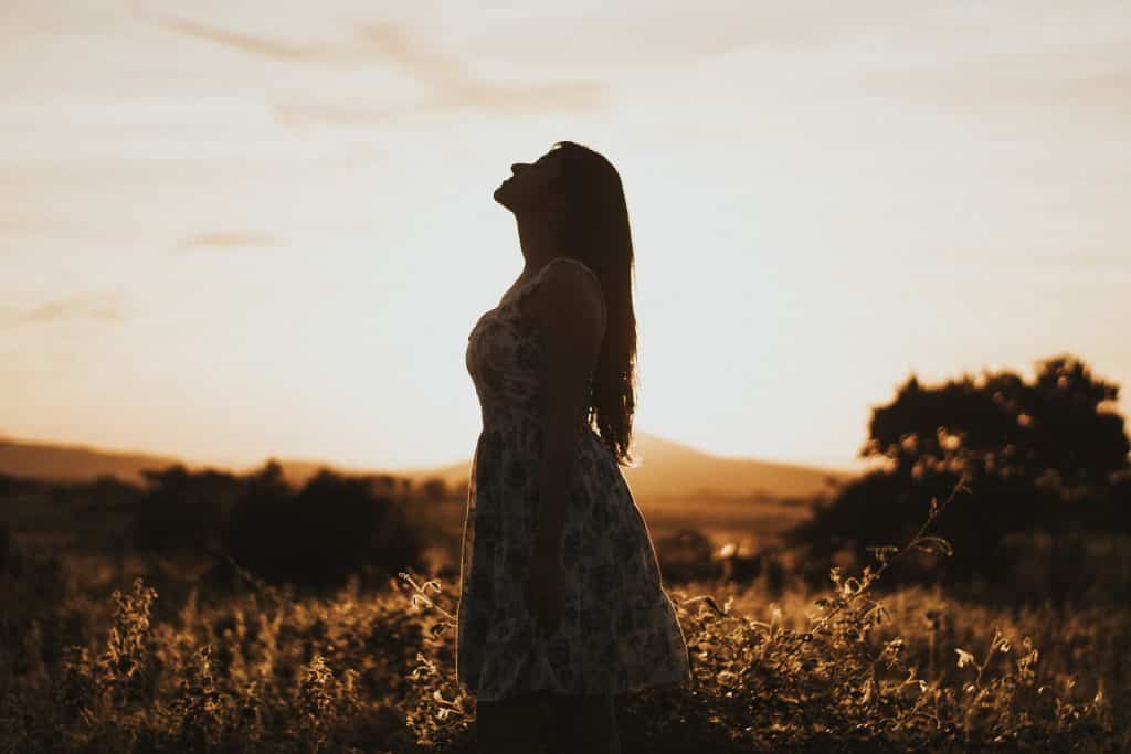 Mulher branca com os olhos fechados e cabeça levantada num campo.