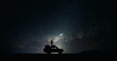 Homem em cima de um carro e o céu estrelado ao fundo.