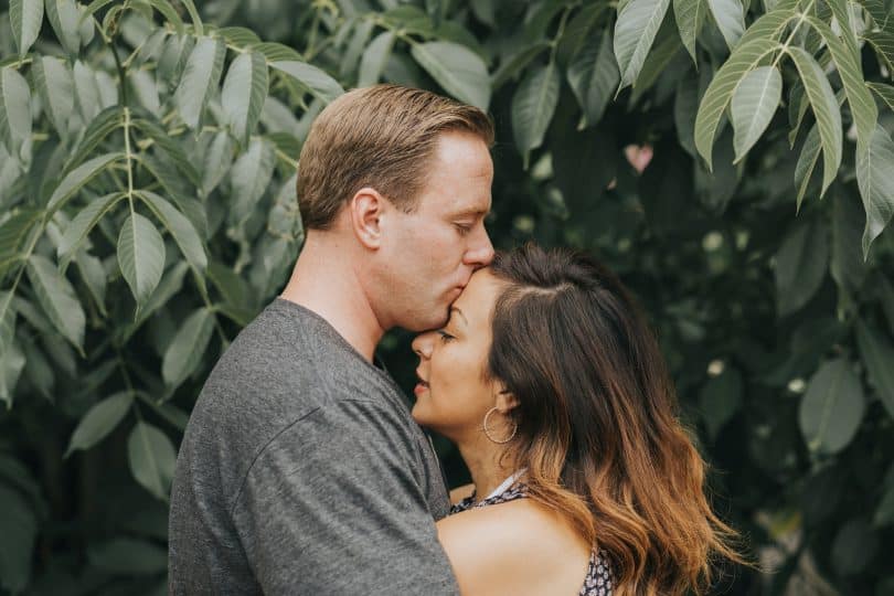 Homem branco beijando testa de mulher branca.