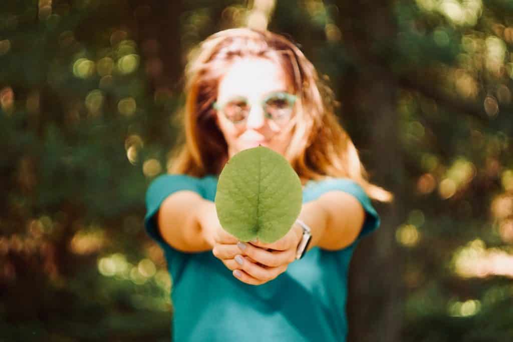 Mulher branca segurando uma folha verde.