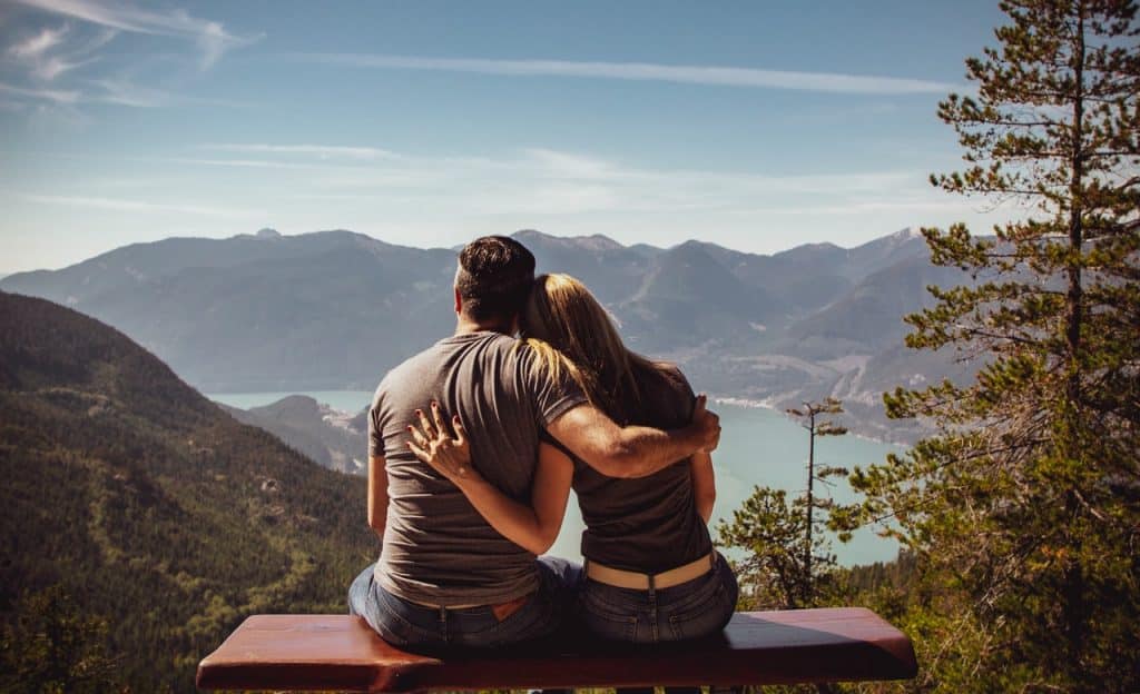 Homem e mulher abraçados sentados sobre um banco de madeira. 