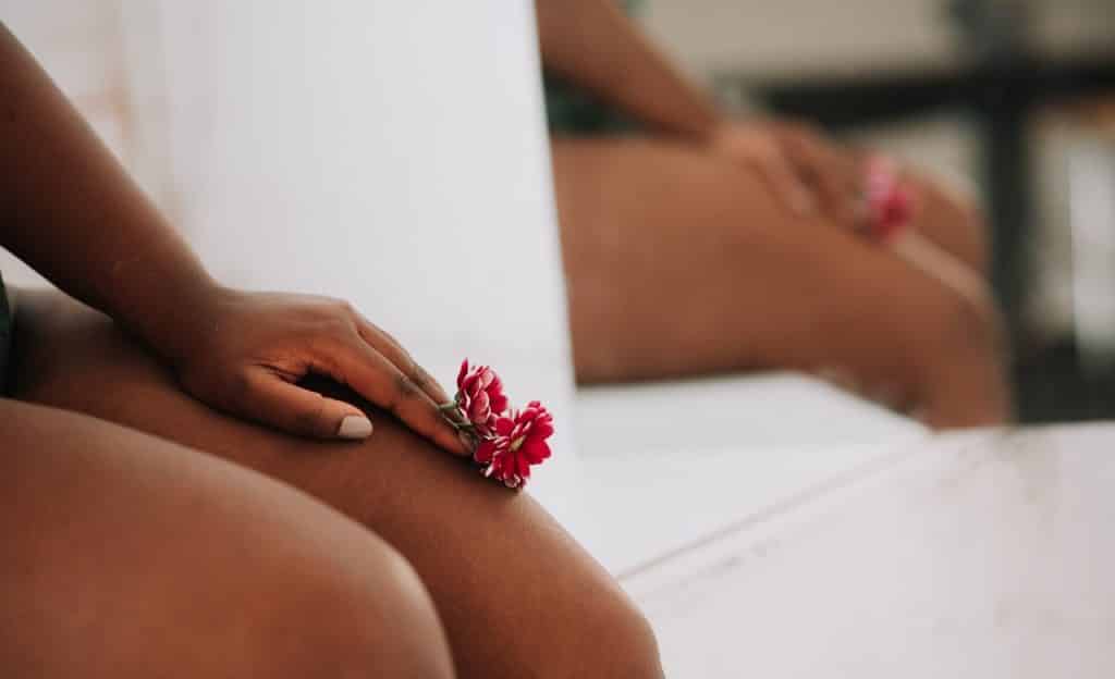 Mulher sentada em superfície branca. Ela segura flores cor de rosa sobre a perna.