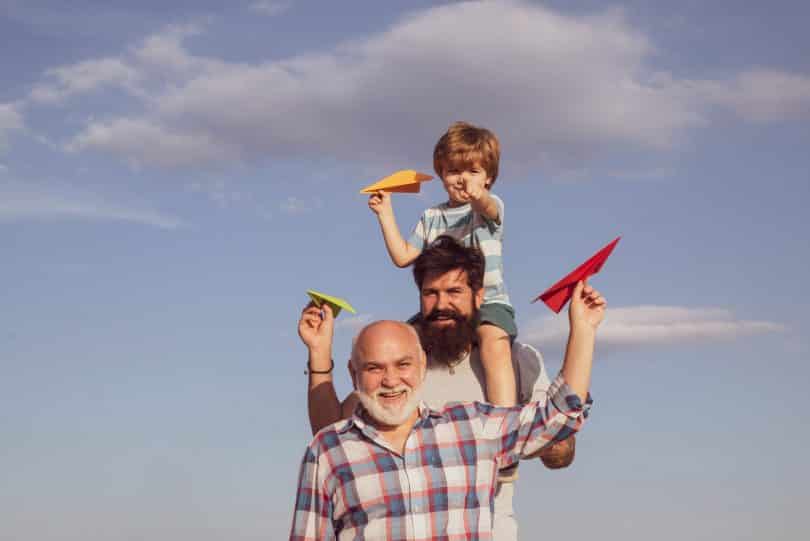 Três diferentes gerações conceituadas a partir de três pessoas: um homem idoso à frente, logo atrás dele um jovem adulto e, sobre os seus ombros, um menino. Os três têm aviões de papel nas mãos.