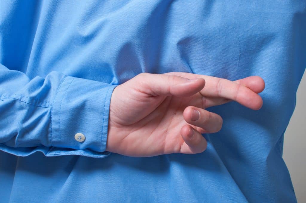 Homem de camisa azul cruzando os dedos atrás das costas