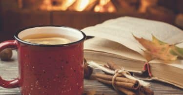 Caneca com chá e livro ao lado.