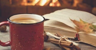 Caneca com chá e livro ao lado.