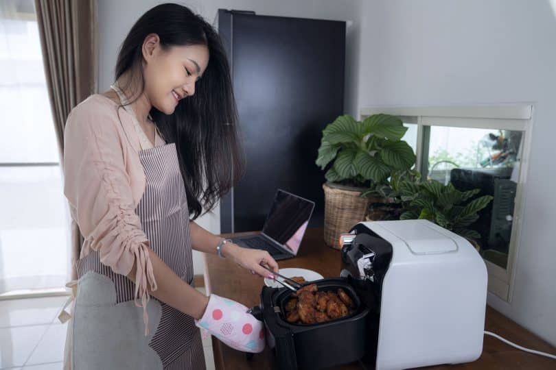 Mulher fritando frango em uma fritadeira elétrica.