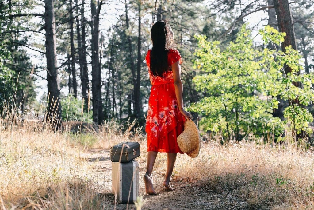 Mulher branca segurando chapéu de palha numa floresta.