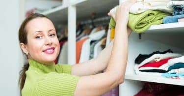 Mulher sorri e organiza roupas em armários.