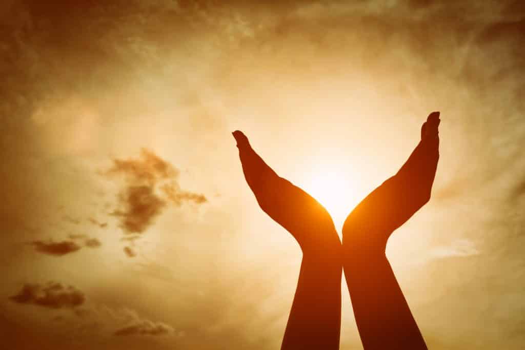 Mãos levantadas, pegando sol no céu do sol. Conceito de espiritualidade, bem-estar, energia positiva etc.