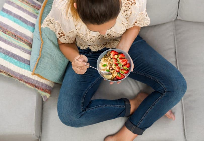 Mulher comendo tigela de frutas.