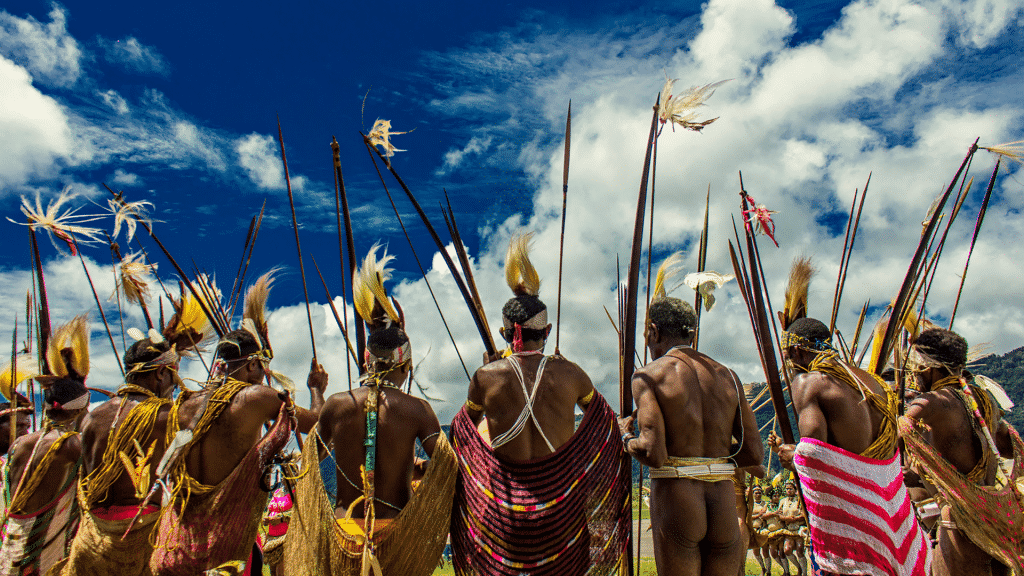Povo indígena segurando lanças um ao lado do outro, de costas